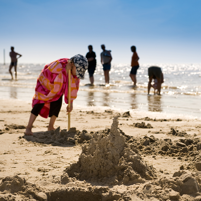 Kind in Handtuch gehüllt spielt mit Schaufel im Sand