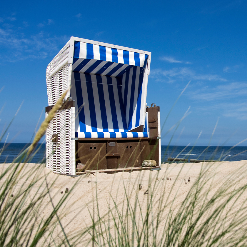 Blau-weißer Strandkorb an der Küste im Sand