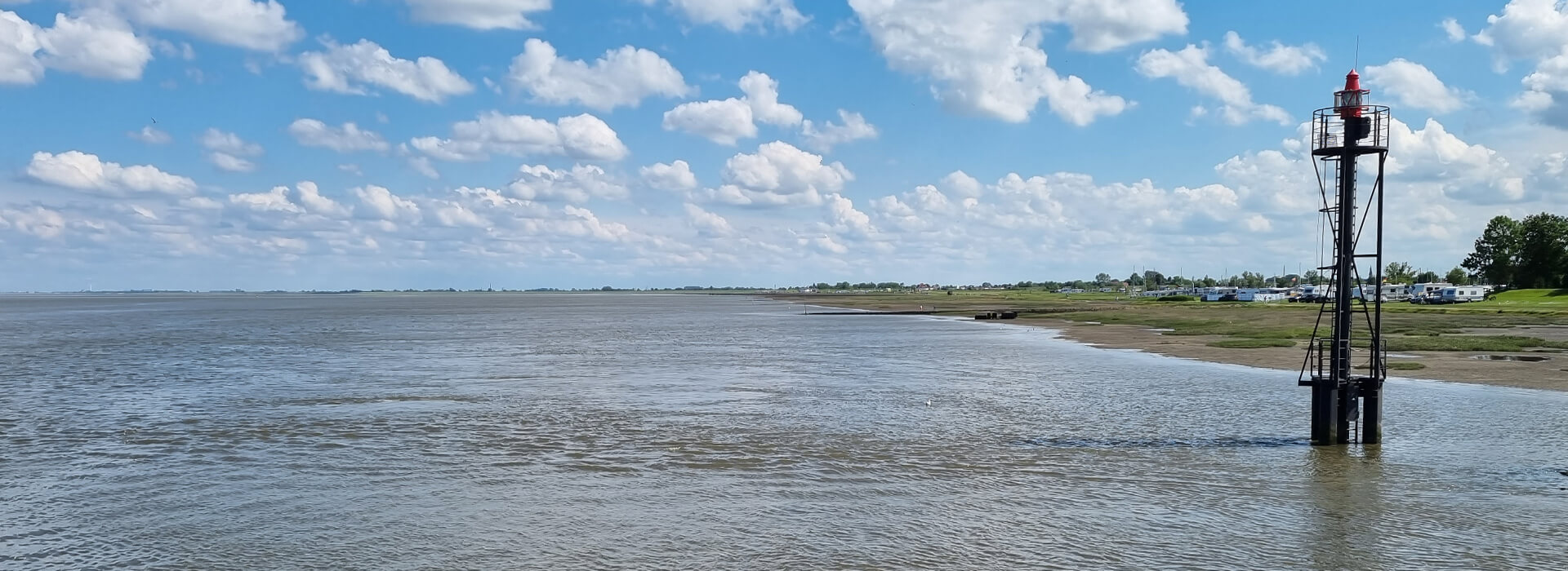 Wasser und grüner Strandabschnitt bei leicht bewölktem Himmel