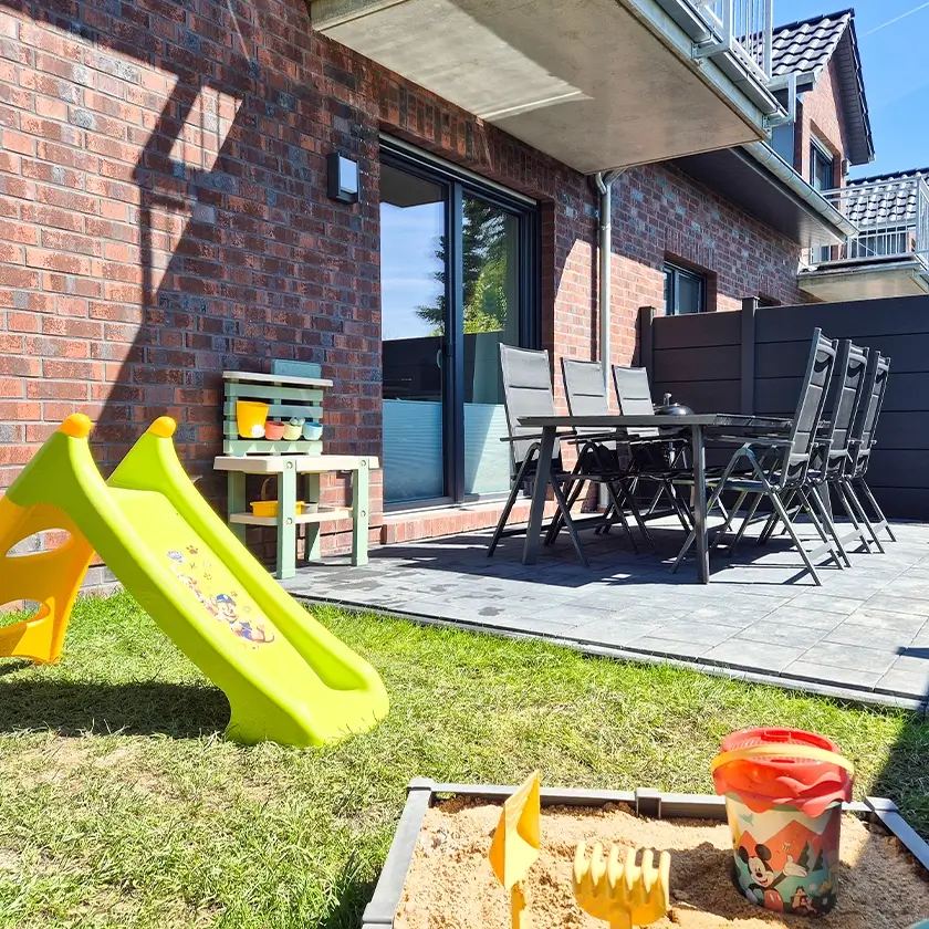 Rutsche und Sandkasten für Kinder, Terrasse mit Mobiliar im Hintergrund