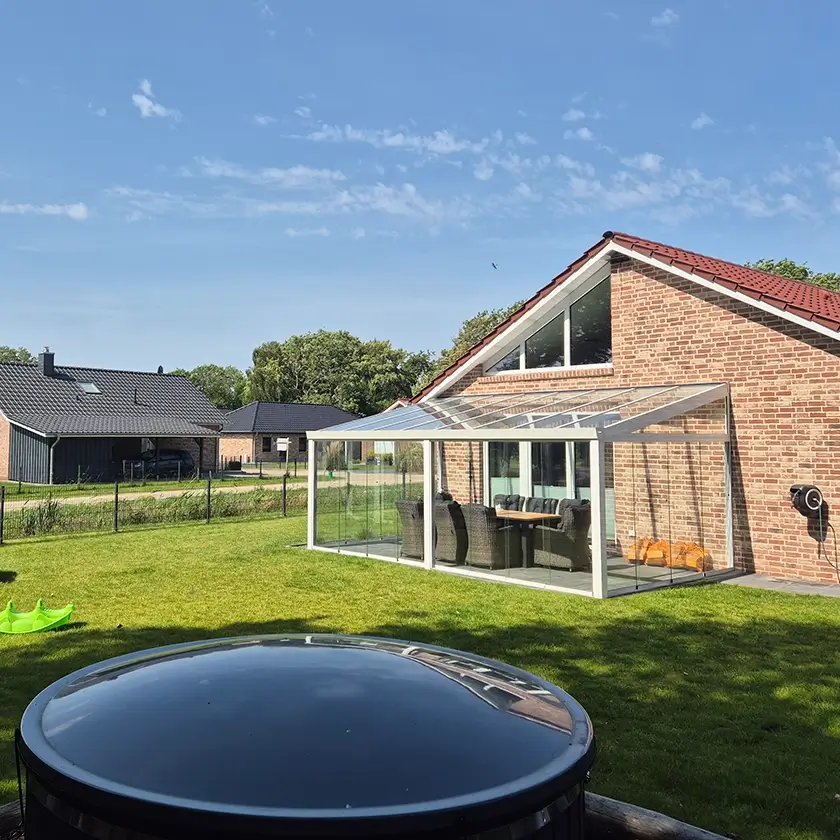 Ferienhaus mit Terrassenüberdachung zum eingezäunten Garten, im Vordergrund abgedecktes Hotfass